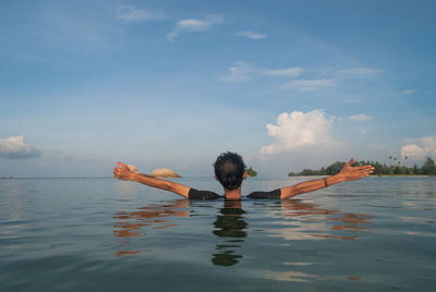 Back view of man standing in sea with arms outstretched