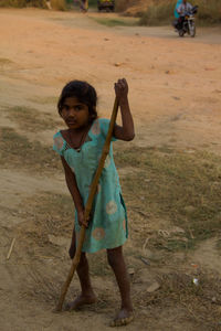 Full length portrait of homeless girl holding stick on field