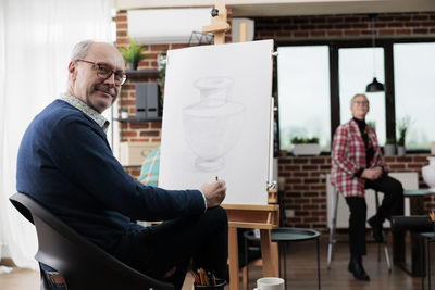 Rear view of man using digital tablet while sitting on chair