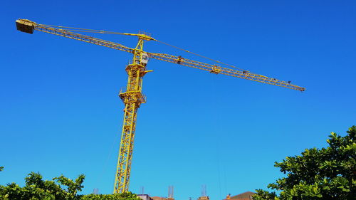 Low angle view of crane against clear blue sky