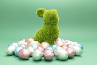 Green bunny, rabbit surrounded by small easter chocolate eggs, sweets wrapped in colorful bright