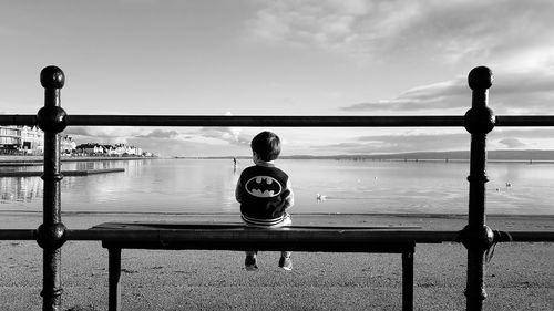 Rear view of boy standing by railing against sky