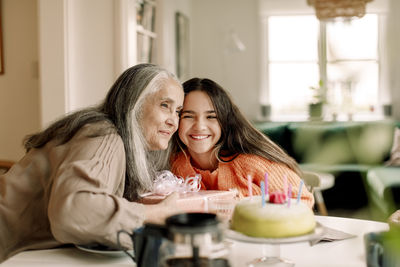 Smiling senior woman and granddaughter with birthday cake at home