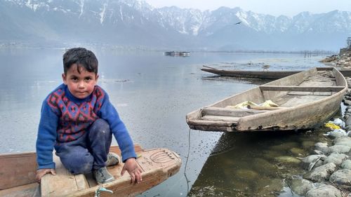 Portrait of boy sitting on boat moored at lake during winter