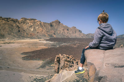 Boy sitting on rock at desert