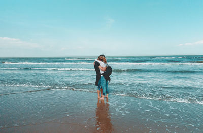 Couple hugging on beach against sky