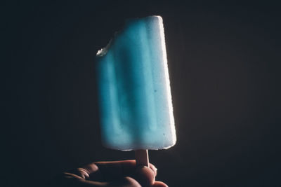 Close-up of hand holding ice cream against black background