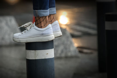 Low section of woman standing on bollard during sunset