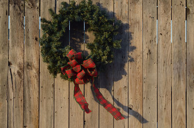Christmas holiday wreath with red plaid ribbon hanging on wooden fence outdoors