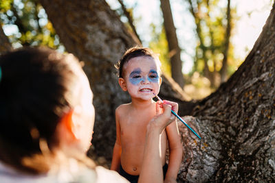 Portrait of shirtless boy holding tree