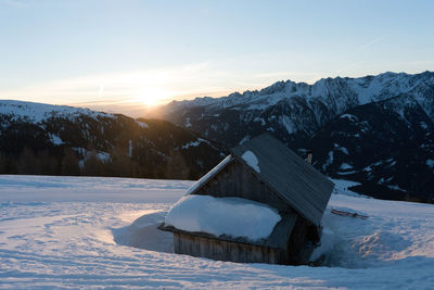 Snow covered landscape against sky during sunset