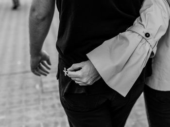 Midsection of woman holding flower while walking with boyfriend on footpath