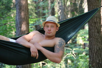 Portrait of young man sitting on hammock in forest