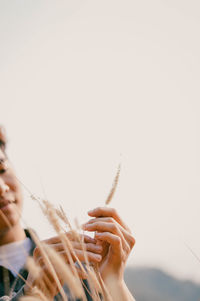 Close-up of hand holding plant against clear sky