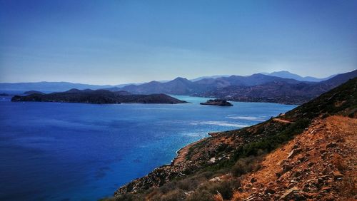 Scenic view of sea and mountains against clear blue sky