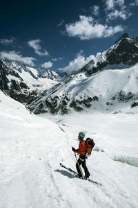 Man with umbrella on snowcapped mountain against sky