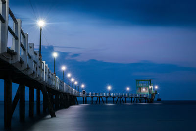 Illuminated pier over sea against sky at dusk
