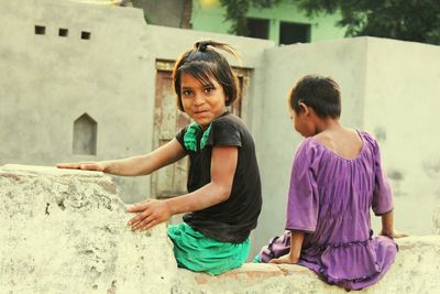 Portrait of smiling girl sitting by friend on wall