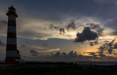Lighthouse by sea against sky during sunset