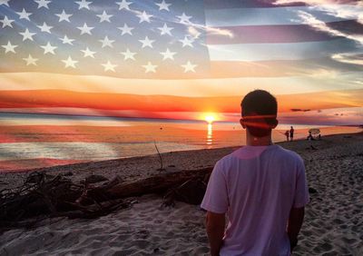 Rear view of man standing at beach during sunset