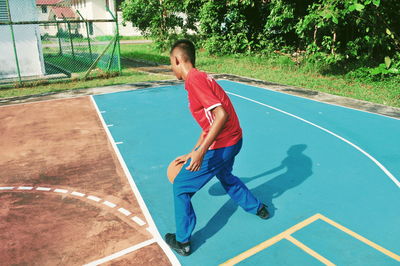 Full length of teenage boy playing basketball on sports court