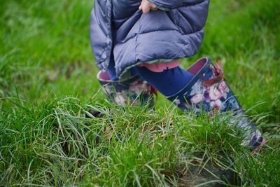 Low section of a little girls with wellies and winter coat on grassy field