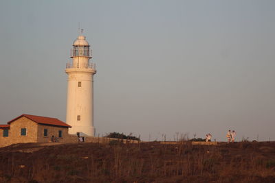 Lighthouse by building against clear sky