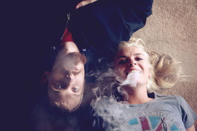 High angle portrait of couple smoking while lying on carpet at home