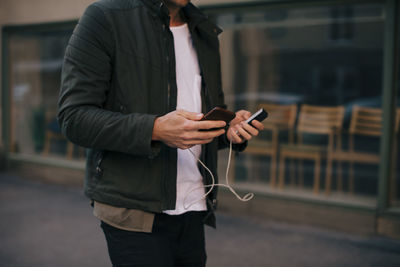 Midsection of man charging smart phone while walking in city