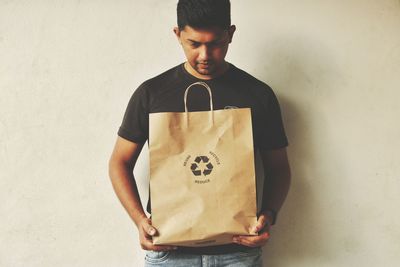 Man with shopping bag standing against wall