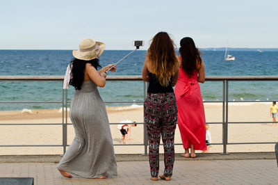 Full length of woman with friends taking selfie at beach