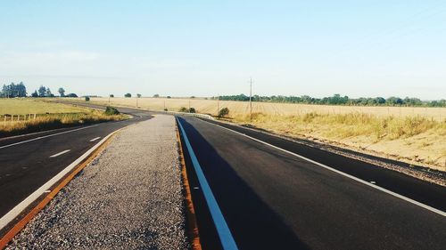 Road passing through field against sky