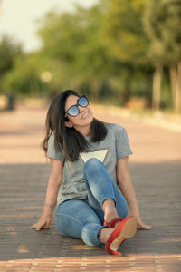 Portrait of woman wearing sunglasses while sitting on boardwalk