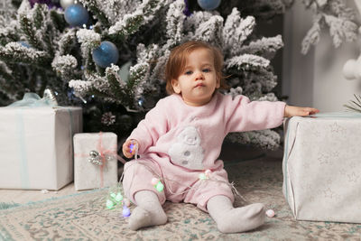 Portrait of cute baby girl sitting against christmas tree