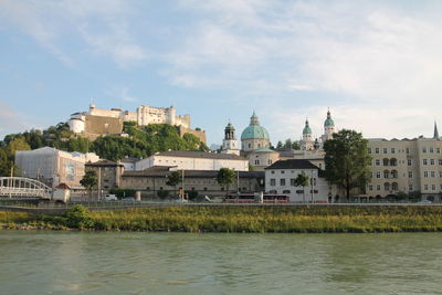 Buildings at waterfront against cloudy sky