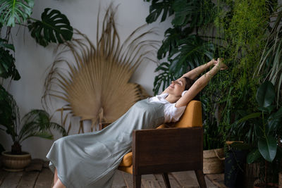 Happy relaxed woman listening music and dreaming with closed eyes while resting in cozy home garden