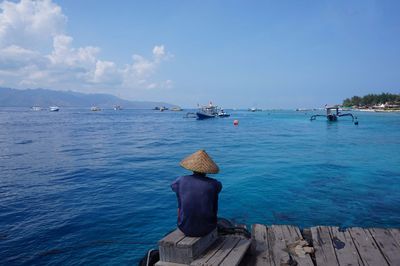 Man sitting on pier against blue sky