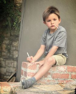 Portrait of boy writing while sitting on retaining wall