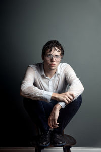 Portrait of young man sitting against wall