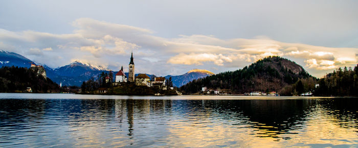 View of buildings by lake against cloudy sky