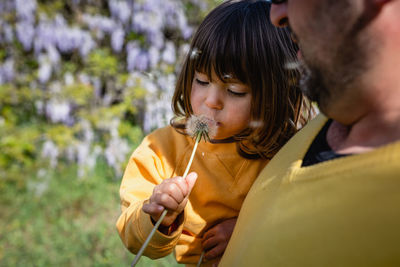 Side view of young kid in yellow clothes blowing flower