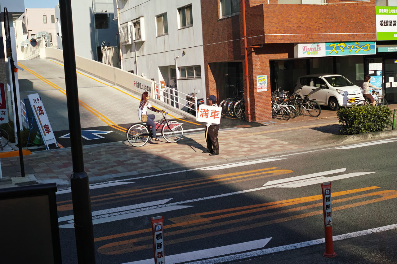 PEOPLE RIDING BICYCLE ON ROAD BY BUILDINGS