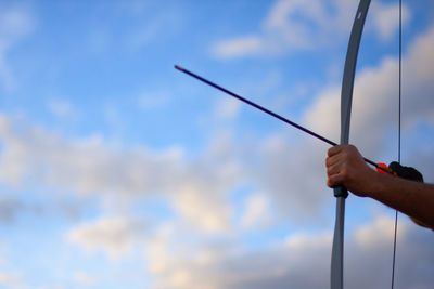 Cropped image of man holding archery bow against sky