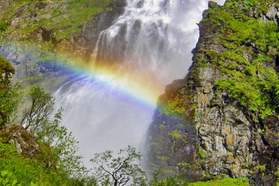 Scenic view of rainbow over rocks and trees