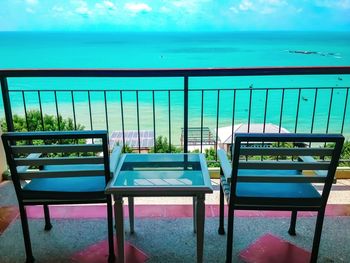 Chairs and table by swimming pool against sea