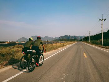 Rear view of men riding bicycle on road against sky