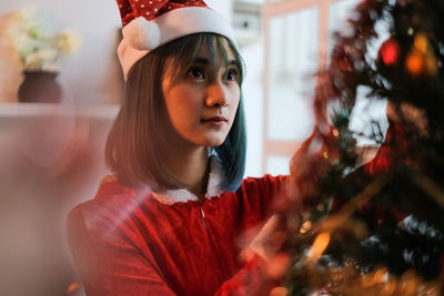 Portrait of young woman looking away at christmas tree