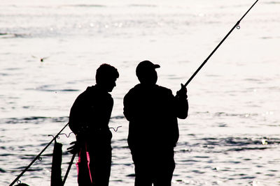 Rear view of silhouette man fishing on beach