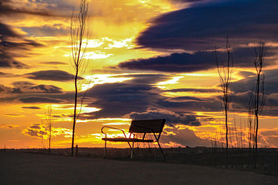 Silhouette chair on beach against sky during sunset