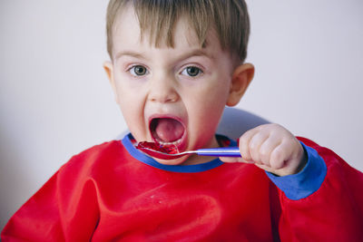 Close-up portrait of cute baby boy eating food against wall